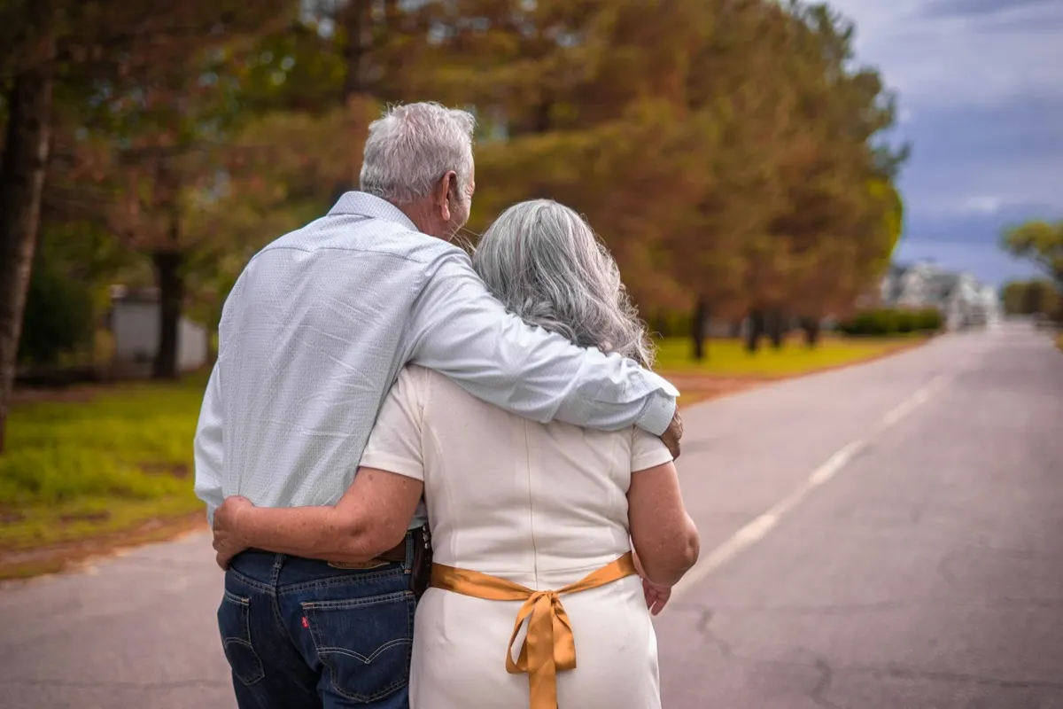 An older married couple walking arm in arm, seen from behind