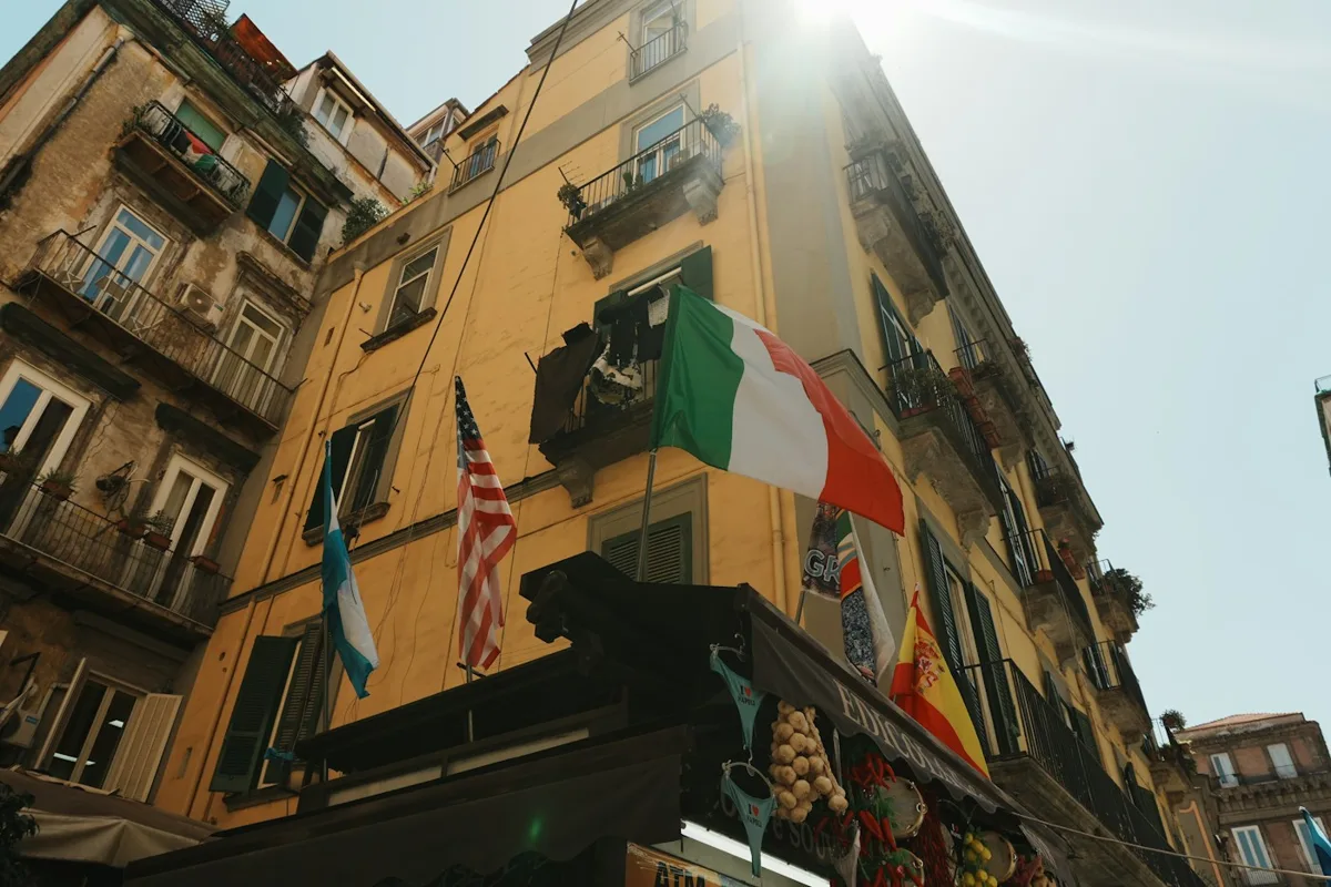 An Italian flag and an American flag flying side by side from a palazzo balcony in Naples