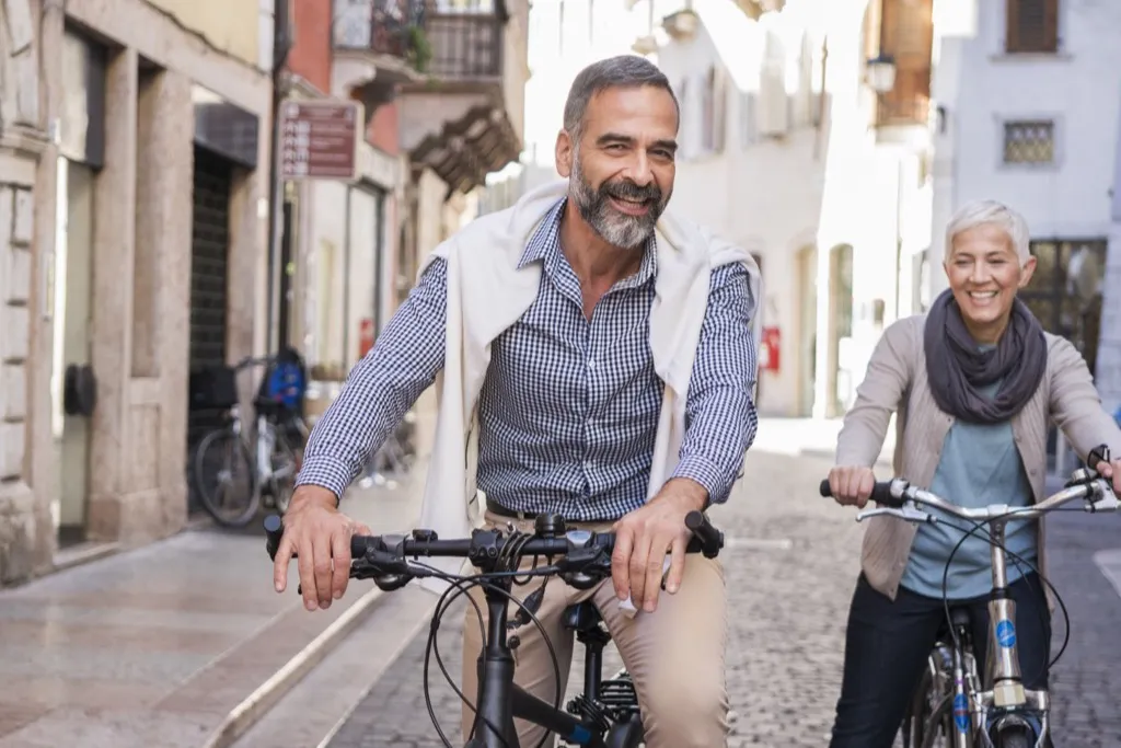 A couple cycling side by side through a narrow Italian street