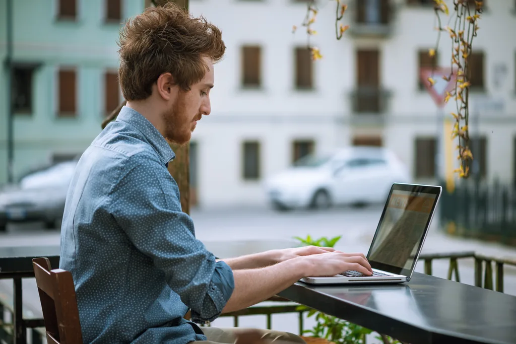 A freelancer typing on a laptop at an outdoor cafe table on an Italian street