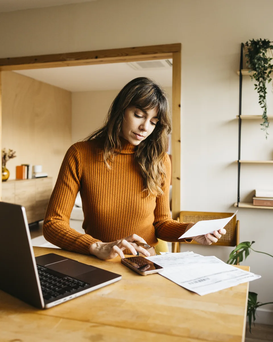 A freelancer at a home-office desk working through a return with a calculator, papers and an open laptop